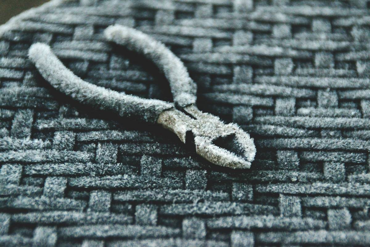 A pair of frosted pliers rests on a textured surface.