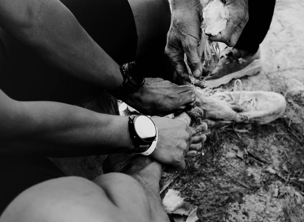 Hands tying muddy running shoes on a dirt path.